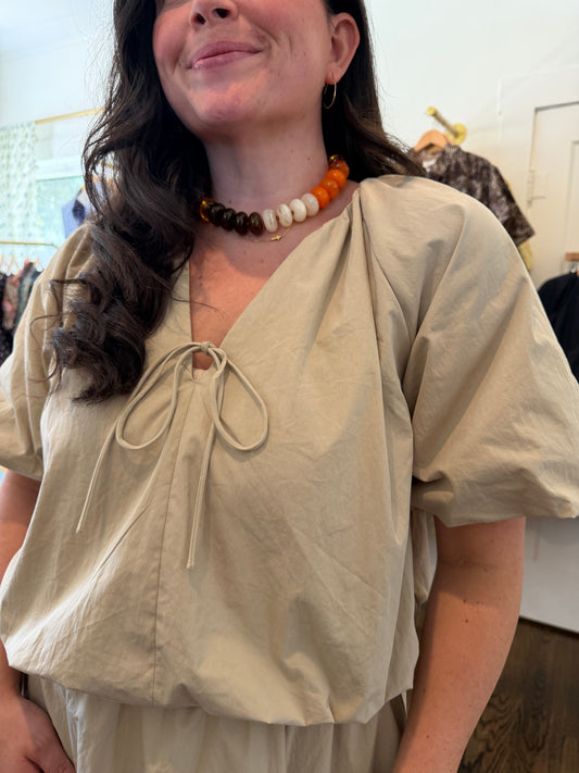 Close view of the Khaki Bubble Set top's tie neck and puff sleeves with a bead necklace