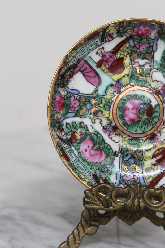 Close view of the Rose Medallion mini plate's pink floral and figure pattern on its brass stand