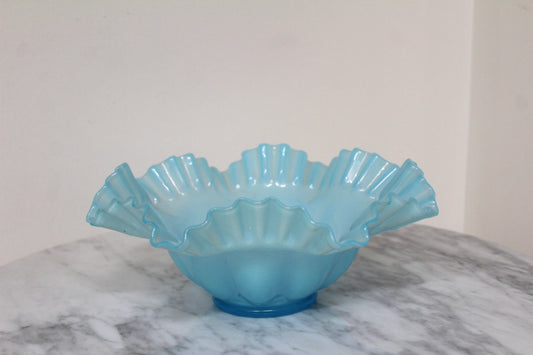 Light blue Fenton ruffle bowl shown from a distance on a marble table