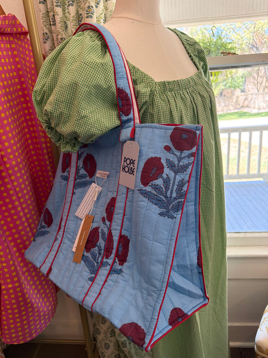 Light blue Milos Tote with a red floral print and red trim, hanging on a dress form