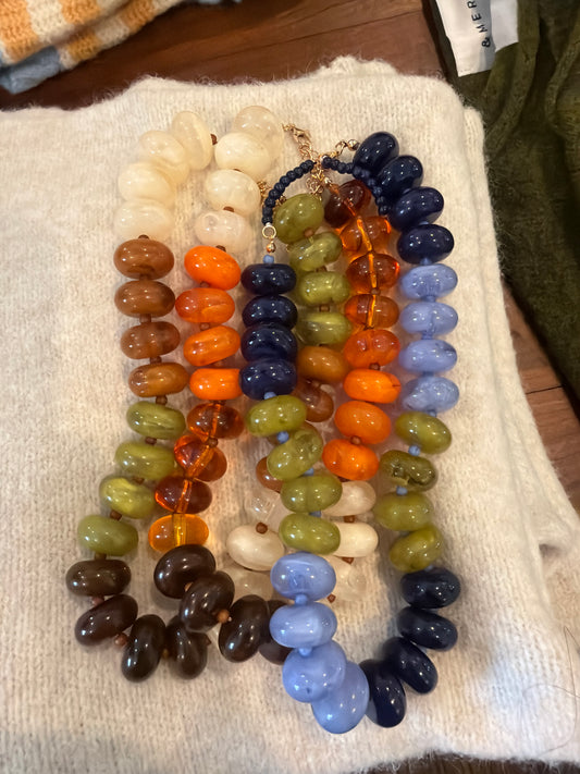 Fall bubble necklaces in cream, orange, green, amber and blue beads laid on a knit blanket