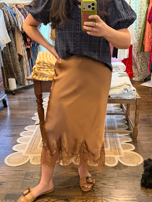 Model taking a close mirror photo in the Mocha Mousse Lace Skirt, a brown satin midi with a lace hem