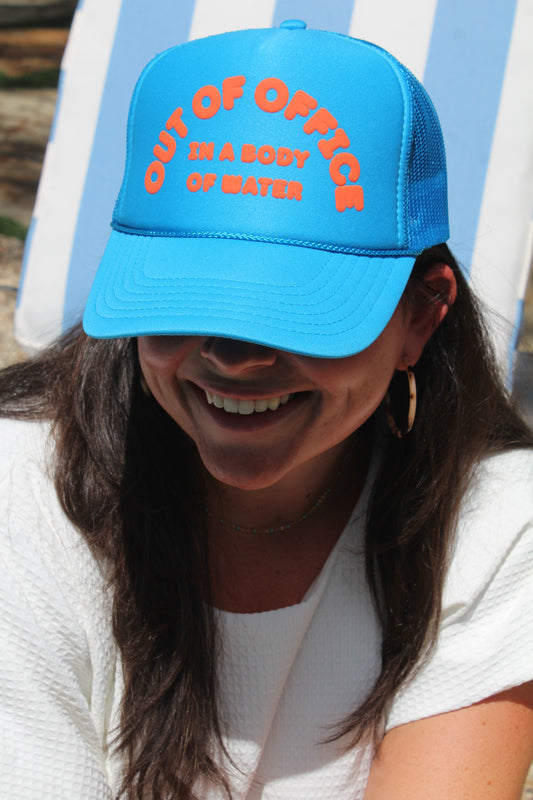 Close view of the blue OOO Trucker Hat that reads Out of Office in a Body of Water in orange