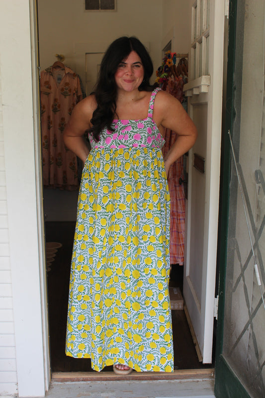 Model wearing the Laguna Sun Dress, a yellow and green floral maxi, in a doorway