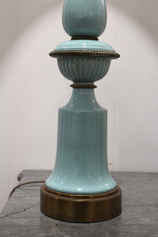 Close view of the vintage blue lamp's light blue ceramic body and brass base, lit